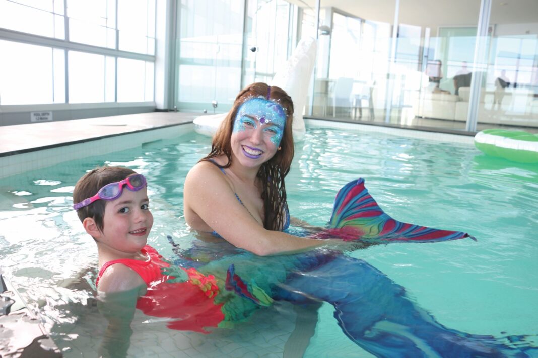 two females in a pool dressed as mermaids