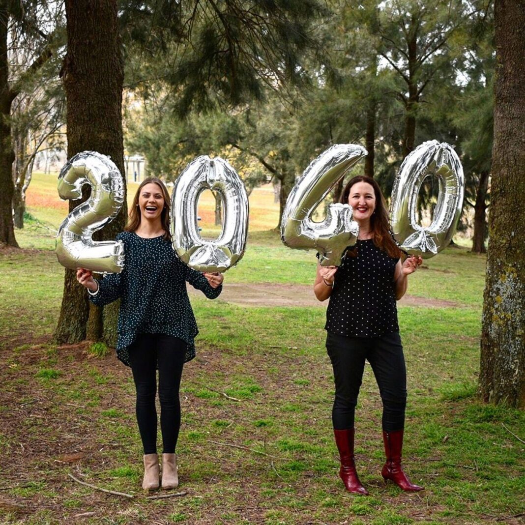 two women holding numbered balloons