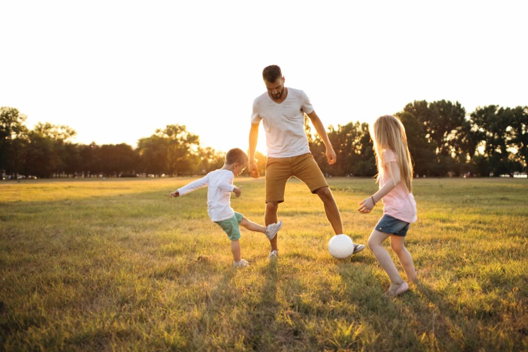 man playing soccer with his two kids