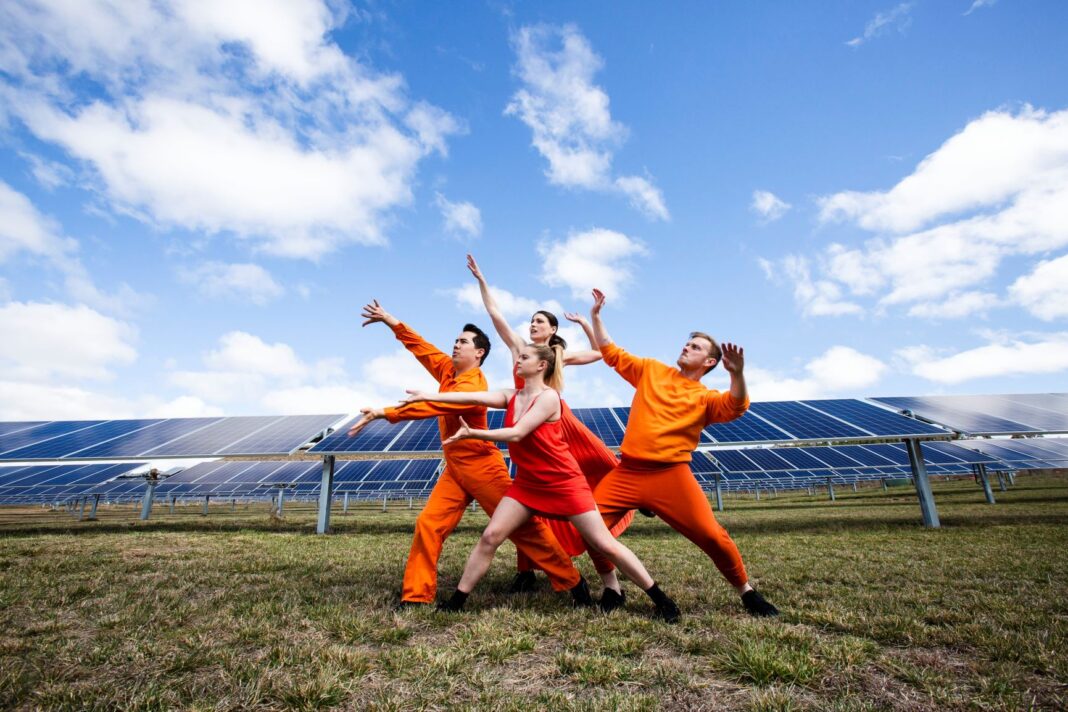 four people posing in front of large solar panels