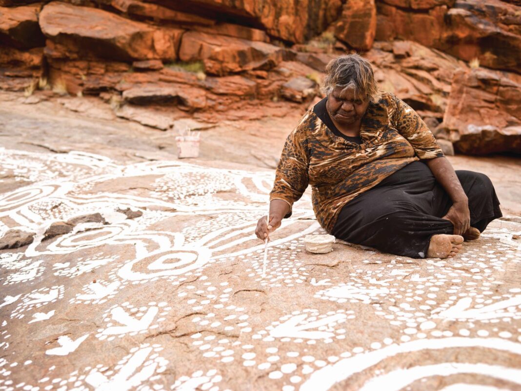 aboriginal woman doing indigenous painting on rocks