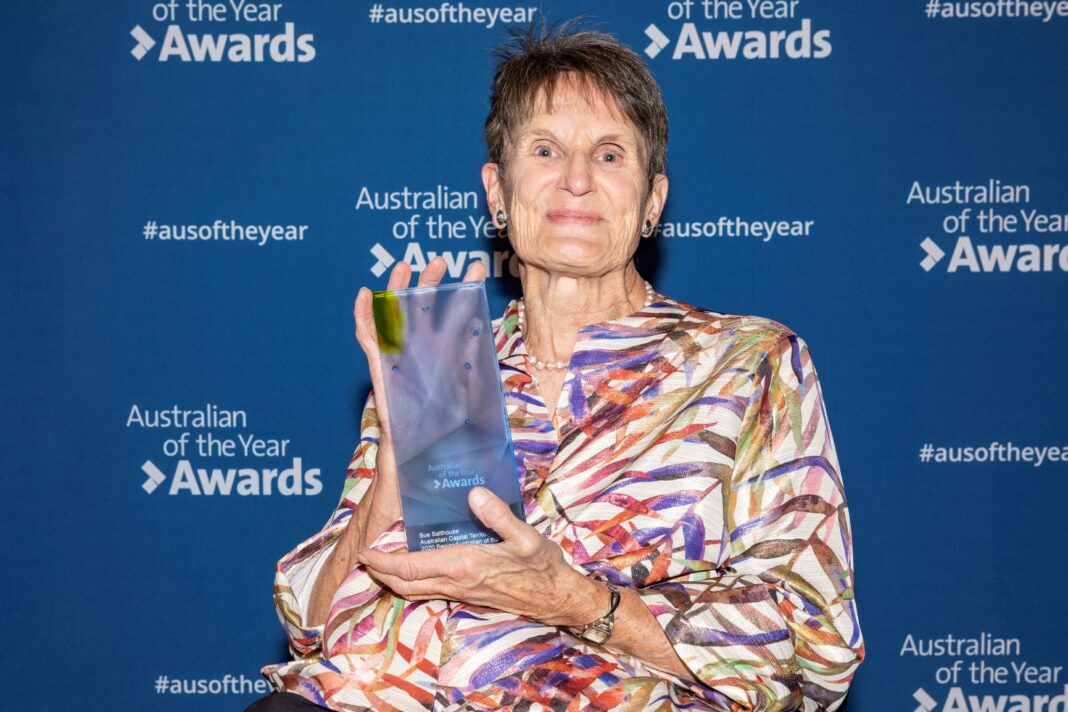 Smiling mature woman in wheelchair holding a glass trophy for the 2020 ACT Senior Australian of the Year award.