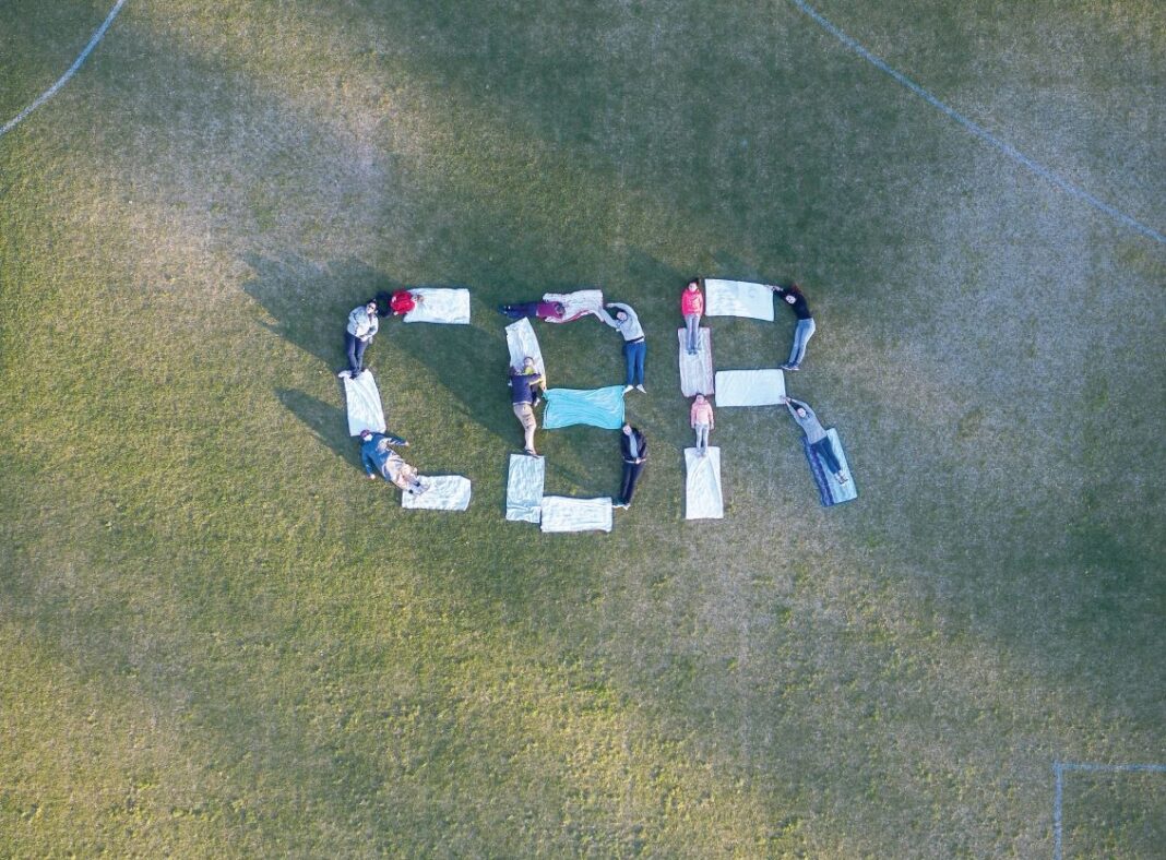 Drone image of people lying on grass forming the letters CBR as seen from overhead