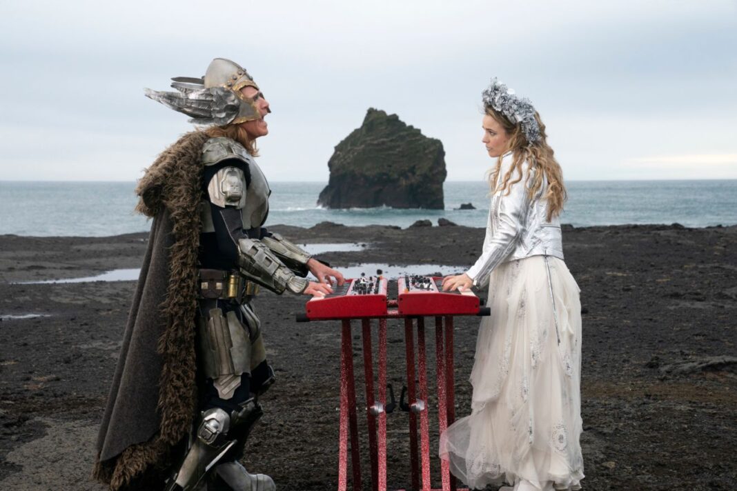 Man in Viking outfit and woman in flowing white gown playing keyboards on a desolate stretch of Icelandic coastline