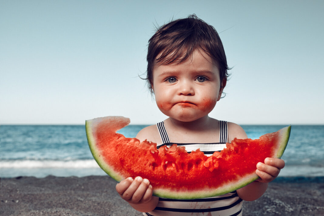 little girl on the beach eating watermelon