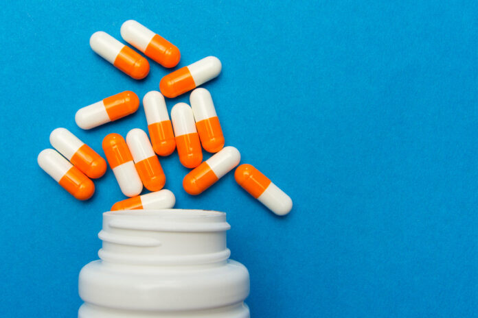 Orange white capsules (pills) were poured from a white bottle on a blue background. Medical background, template.