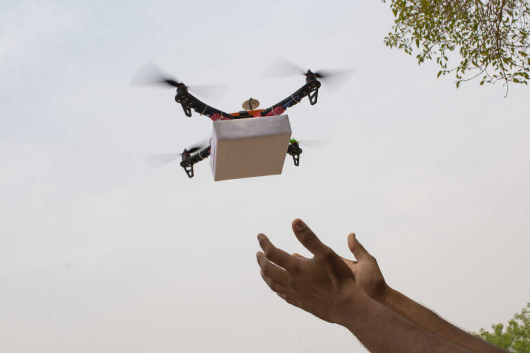 Assembled Drone quadcopter delivering a package and hands receiving the parcel