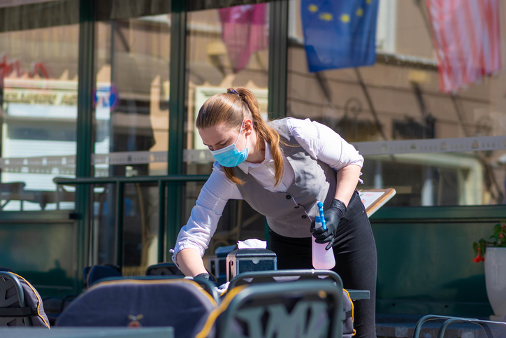 Waitress with a mask disinfects the table of an outdoor bar, café or restaurant, reopen after quarantine restrictions