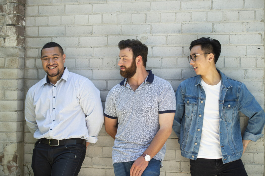 Three mixed race males lined up against brick wall