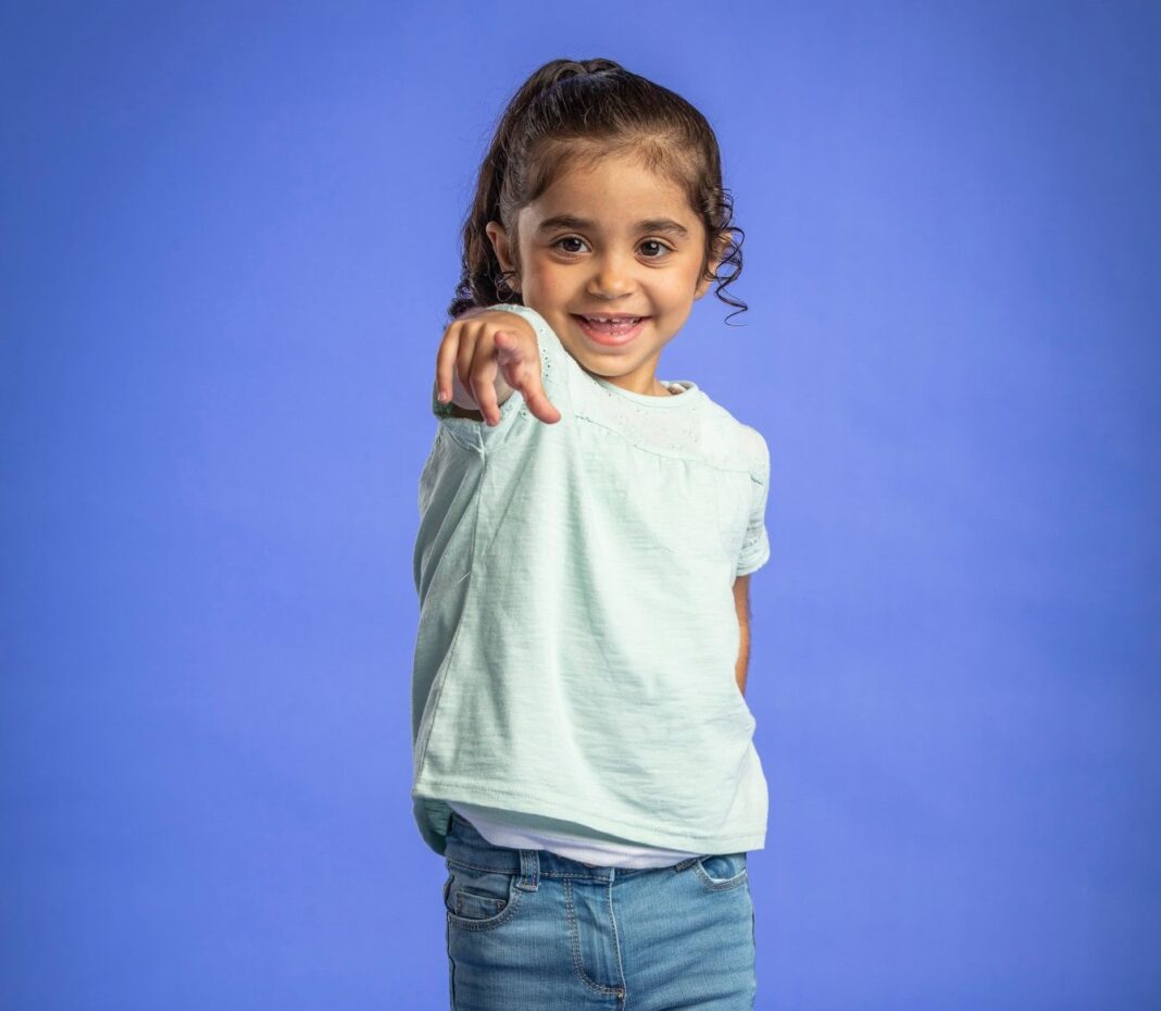 Happy little girl in jeans and T-shirt pointing at the camera