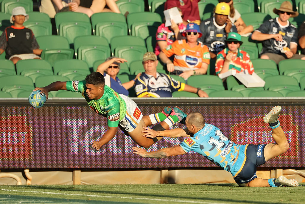 Rugby league footballer in green jersey sailing through the air to score a try as an opposition player in a blue jersey attempts to tackle him