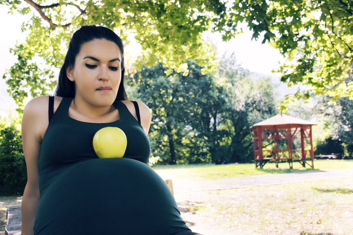 young pregnant woman resting an apple on her baby bump