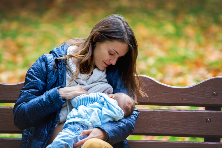 Young mother, breastfeeding her newborn baby boy outdoor in the park, autumn time.