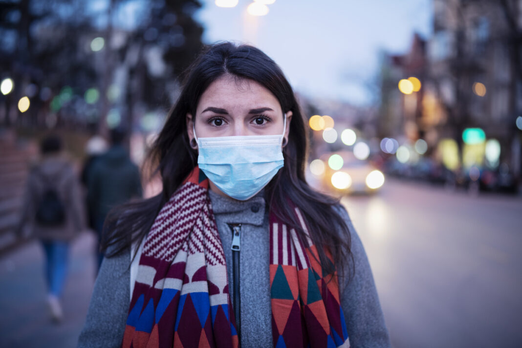 Close up portrait of Latino young woman on the street, she walking on the street with protective face mask and looking at camera, she looking sick and scared.