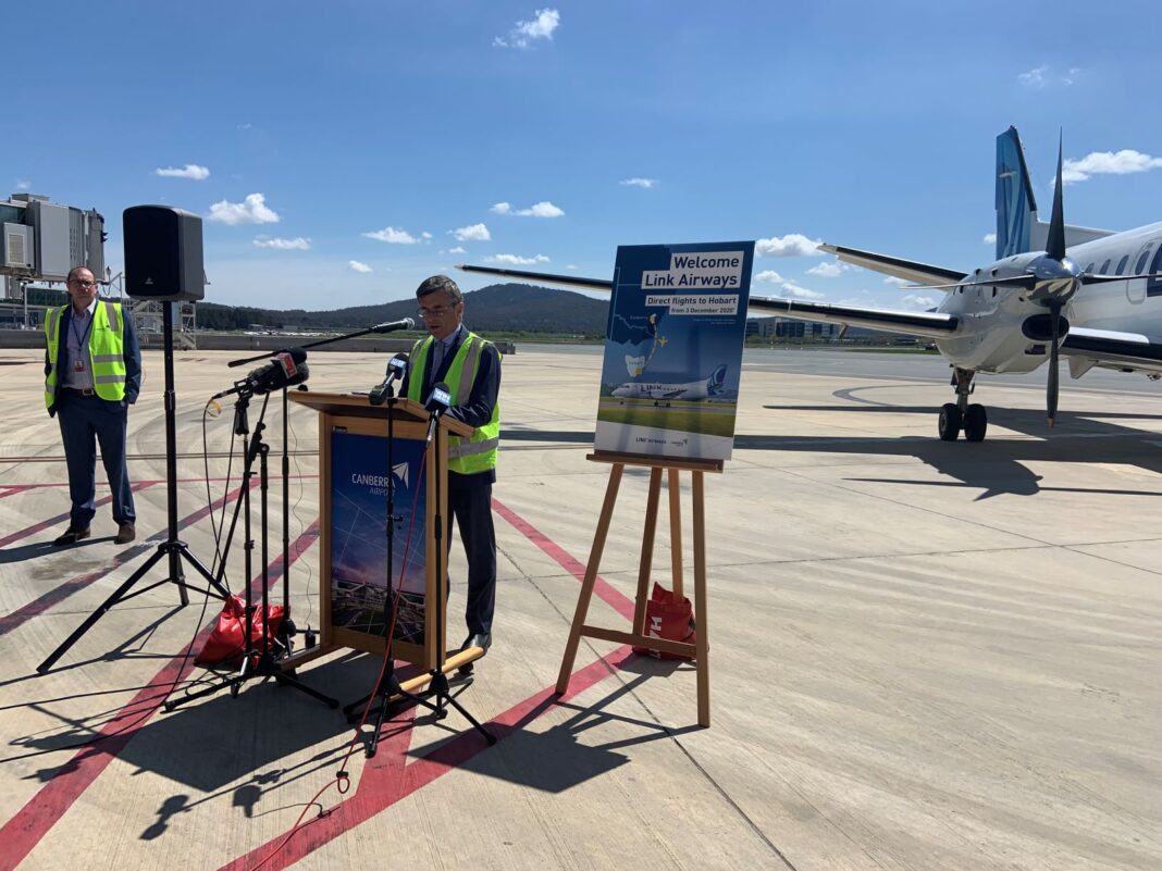 man making an announcement at canberra airport with an aeroplane in the background