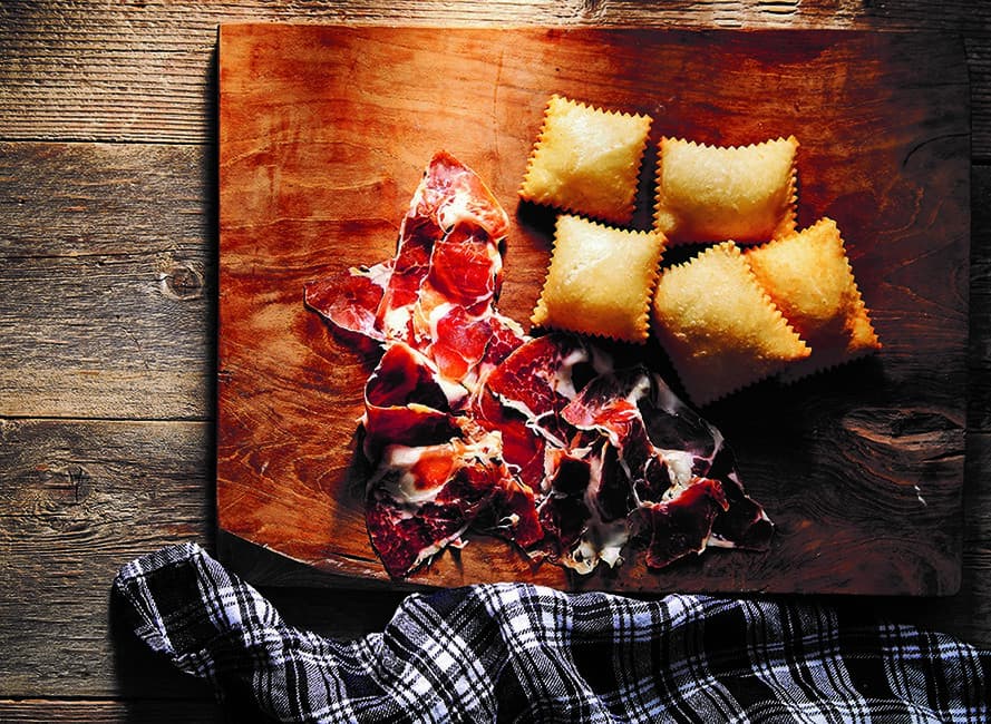 Gnocco fritto on a wooden board served with prosciutto