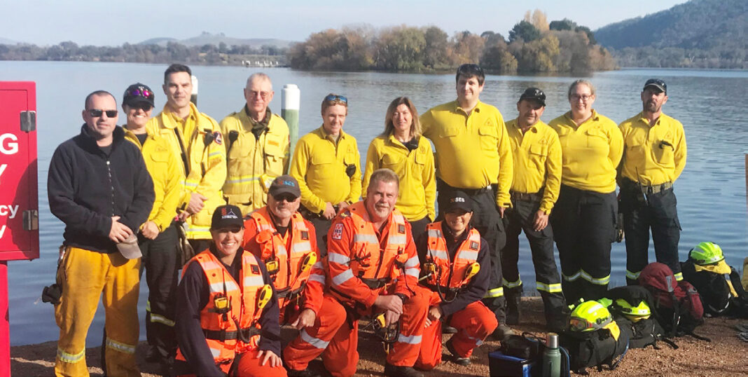 Group of around 12 male and female volunteers in yellow and orange Emergency Services outfits