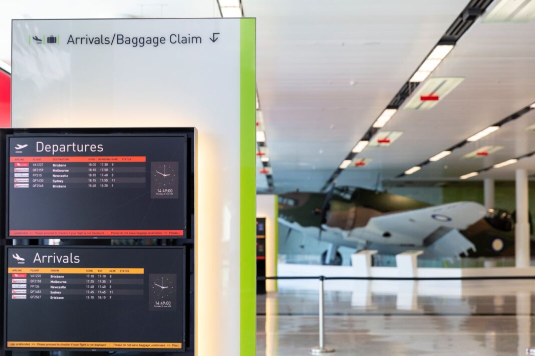 departures board inside Canberra Airport with small plane in background