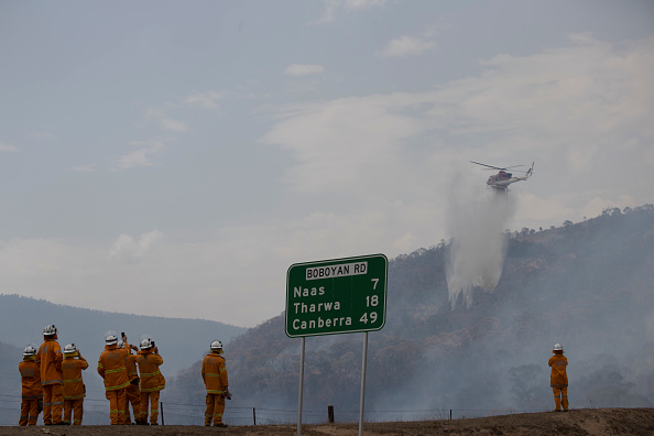 Firefighters watch as a helicopter water bombs a spot fire in the Orroral Valley on Boboyan Road in February 2020.
