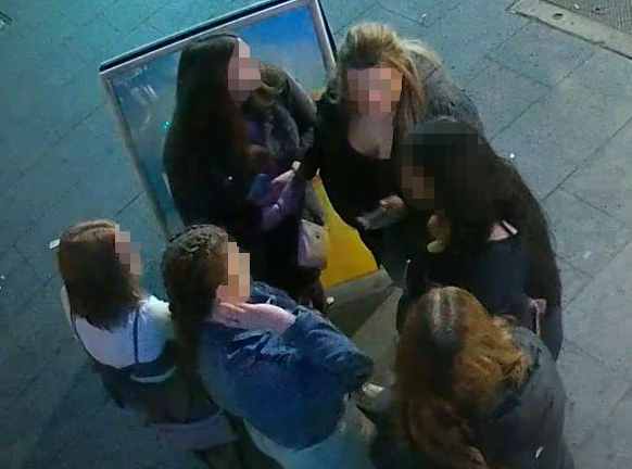 Group of women standing on footpath, faces pixelated to obscure their identity.