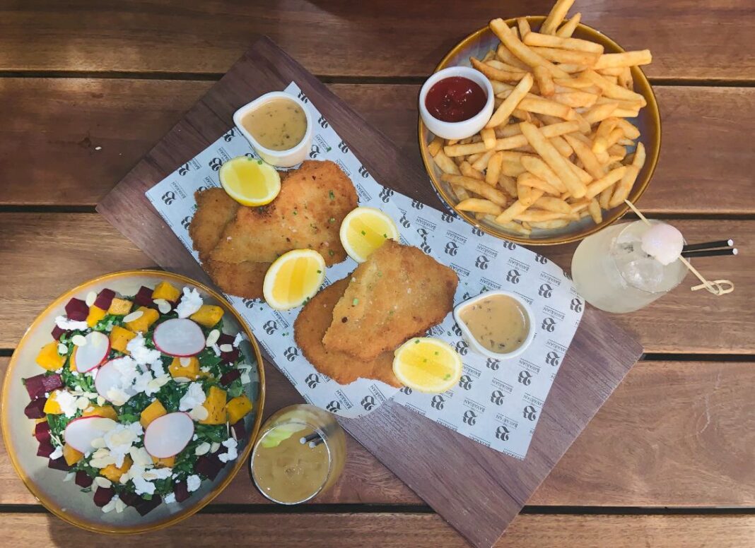 Chicken schnitzels on a table with a plate of hot chips and a bowl of pumpkin and beetroot salad.