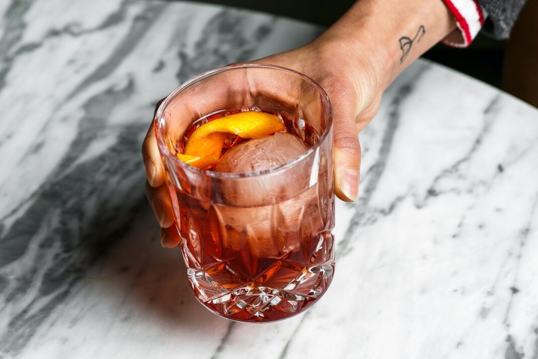 A hand holds a negroni cocktail over a marble table
