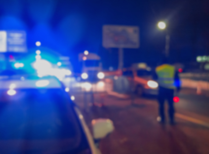 Unrecognizable blurry police car lights and police force officer on night road background, crime scene, night patrolling the city. Abstract defocused image