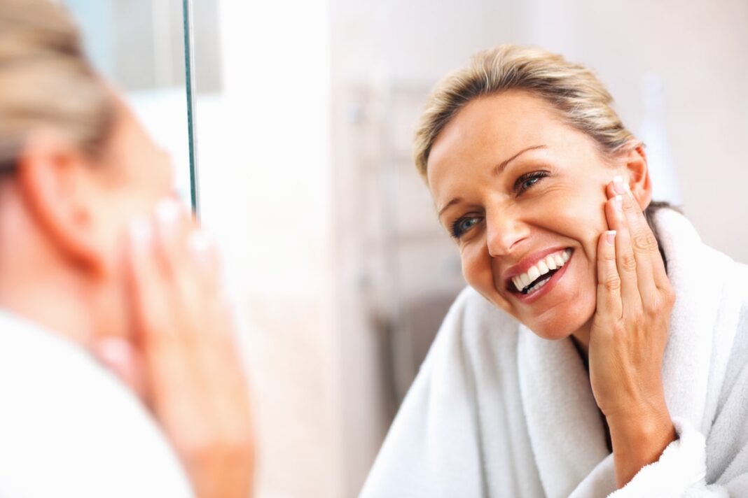 woman looking in the mirror touching her face and smiling