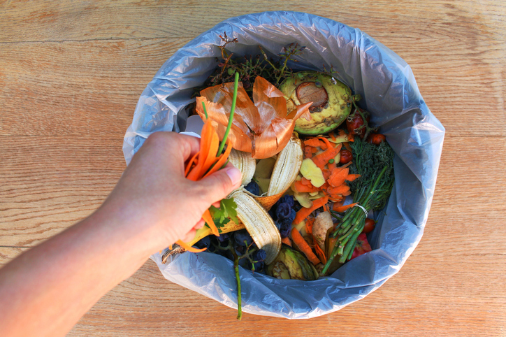 A hand throws food waste into a bin filled with food scraps for compost.