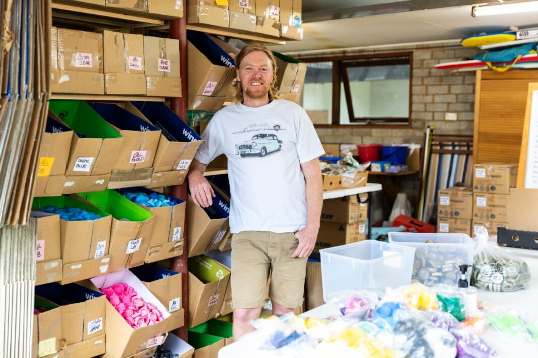 Lids4Kids founder Tim Miller stands in a garage full of boxes of bottle tops