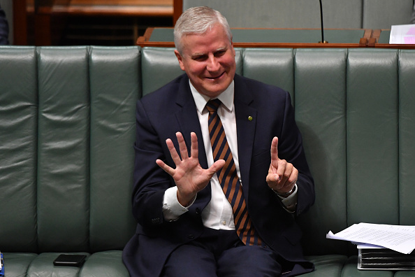 Mature man in suit and tie holding up six fingers sitting on a green bench in the Australian Parliament House of Representatives