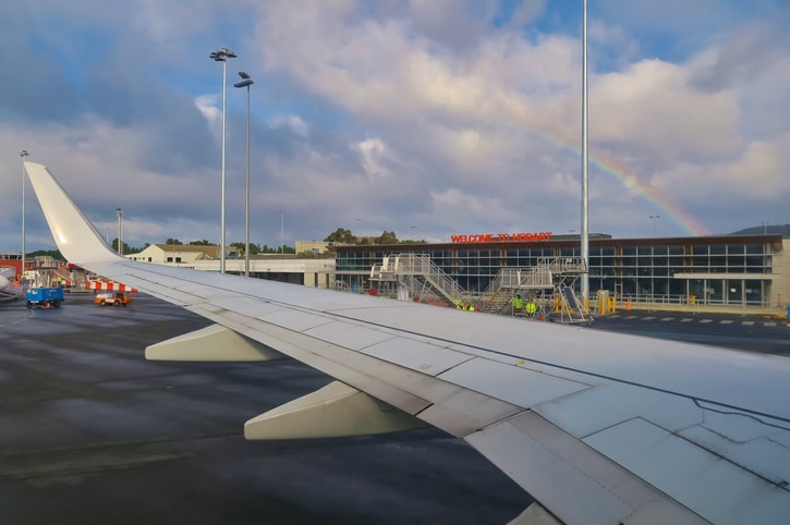 Airplane wing with rainbow and Hobart Airport building is in the background.