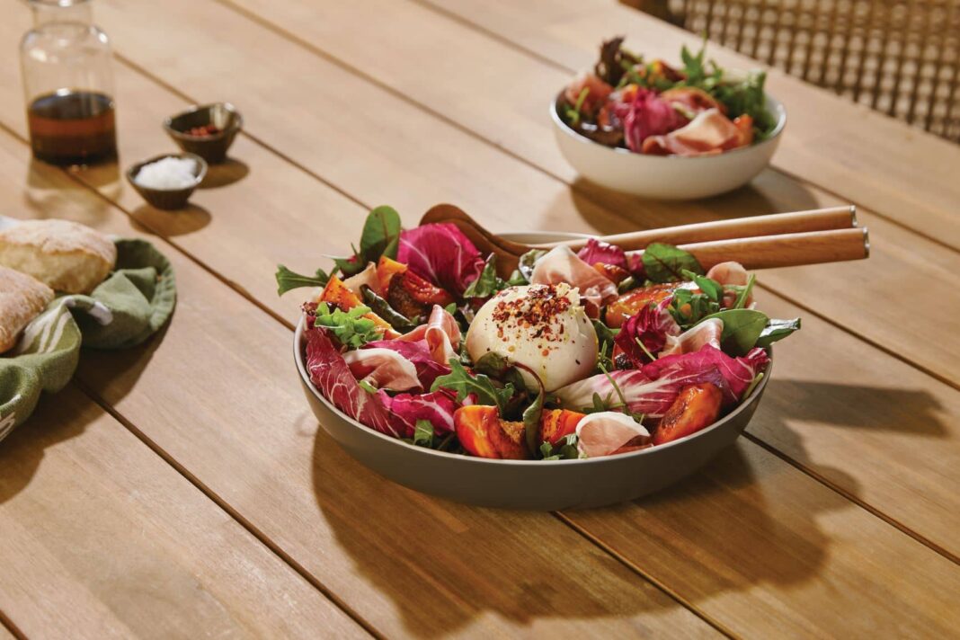BBQ grilled peach, prosciutto and burrata salad in a bowl on a wooden table