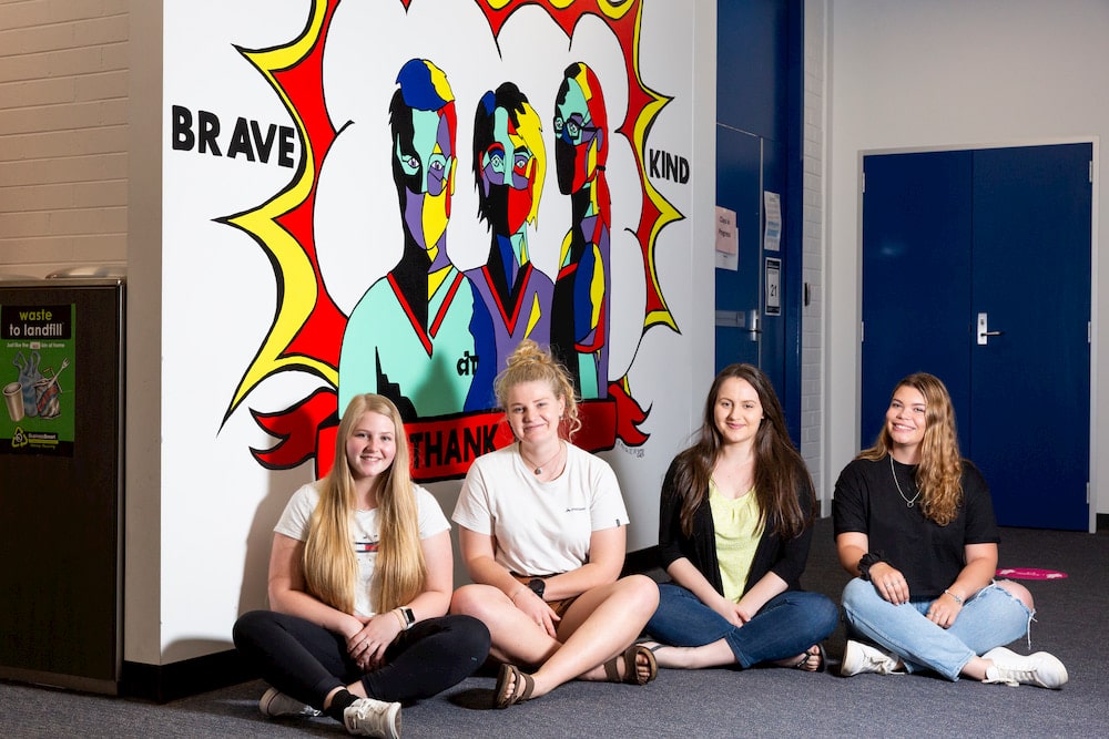Students from CIT Bruce sit in front of a colourful mural they painted to inspire nursing students