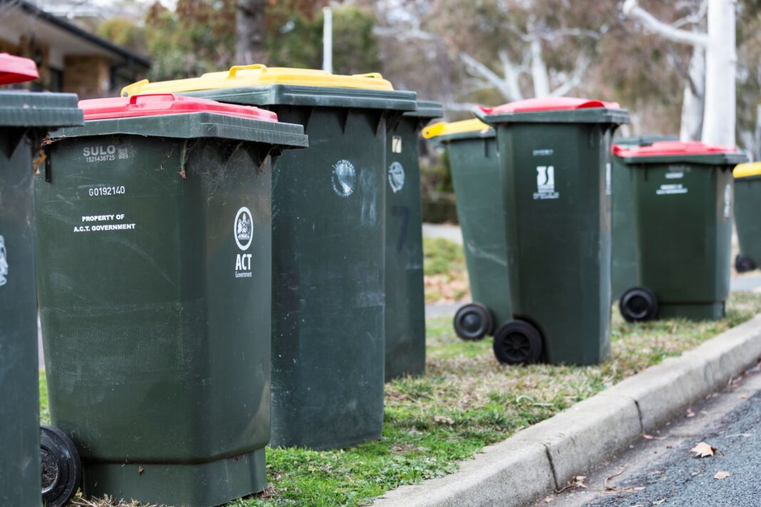 green wheelie bins with red lids and yellow lids lined up along the kerb
