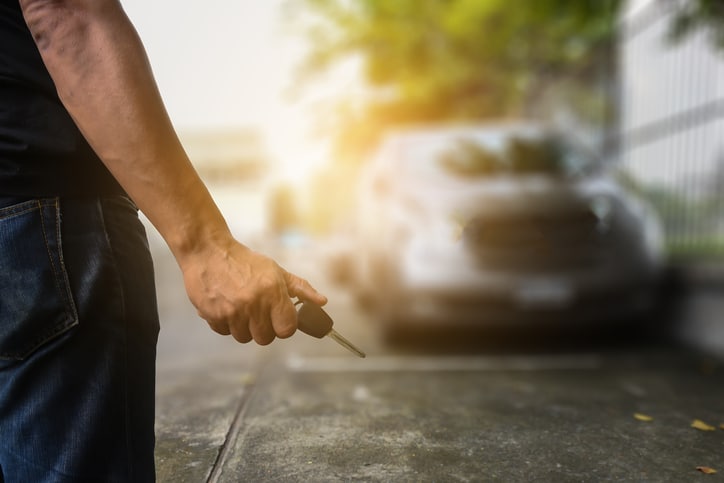 male hand holding car key approaching a parked vehicle in the background