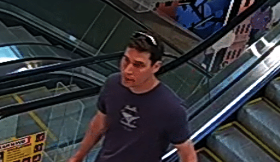 A man in a dark shirt and cargo shorts on an escalator in the Canberra Centre.