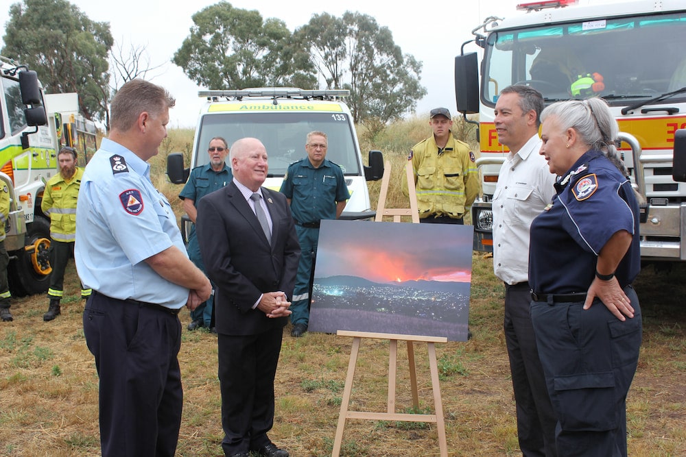Rohan Scott, ACT Rural Fire Service chief officer; Mick Gentleman, Minister for Police and Emergency Services; Daniel Iglesias, ACT Parks and Conservation executive branch manager; and Georgina Whelan, ACT Emergency Services Agency Commissioner, with RFS member Gary Hooker’s photograph of the fire, surrounded by emergency service representatives.