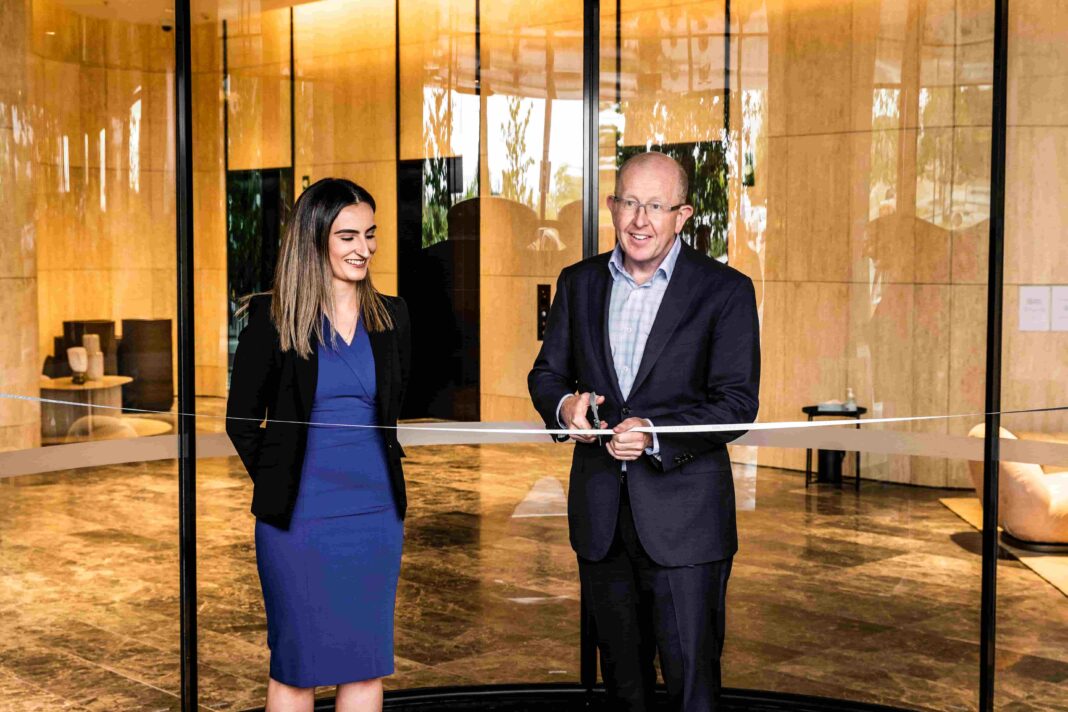 middle aged man cutting ribbon in a shiny new hotel foyer as woman in blue dress looks on