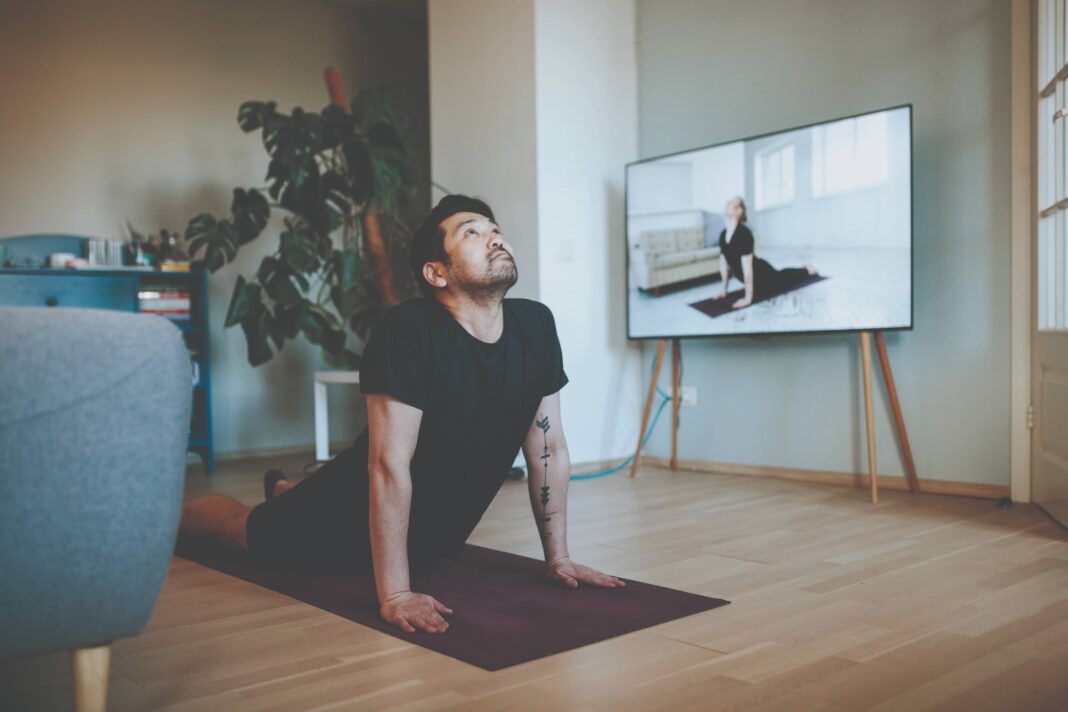 A man does yoga in front of the television during quarantine.