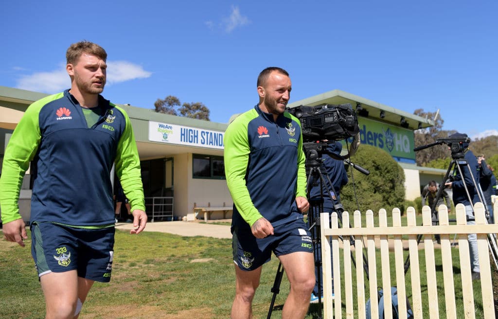 Two Raiders footballers in blue and green training gear walking on an oval