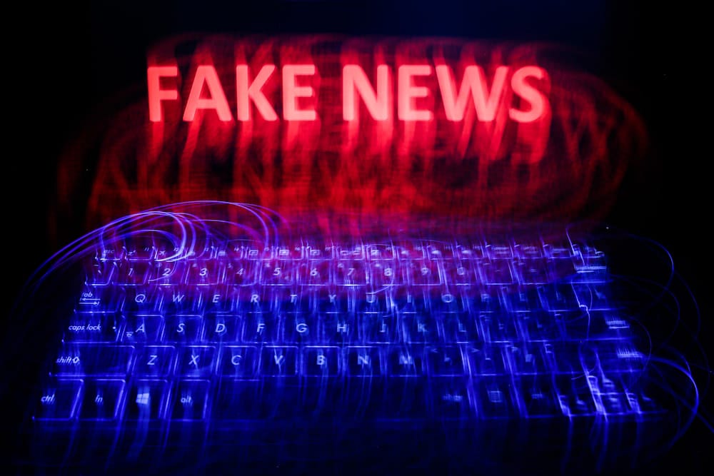 Fake news is written in glowing red capital letters against a black backdrop, and above a glowing blue keyboard. The whole picture is slightly blurry due to a long exposure.