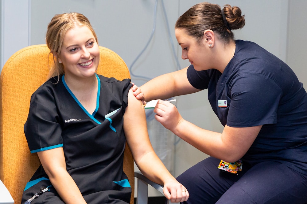 Maddy Williams receives the first coronavirus vaccination at the Garran COVID-19 surge centre, administered by Nikoletta Karagiannidis. Picture: Kerrie Brewer