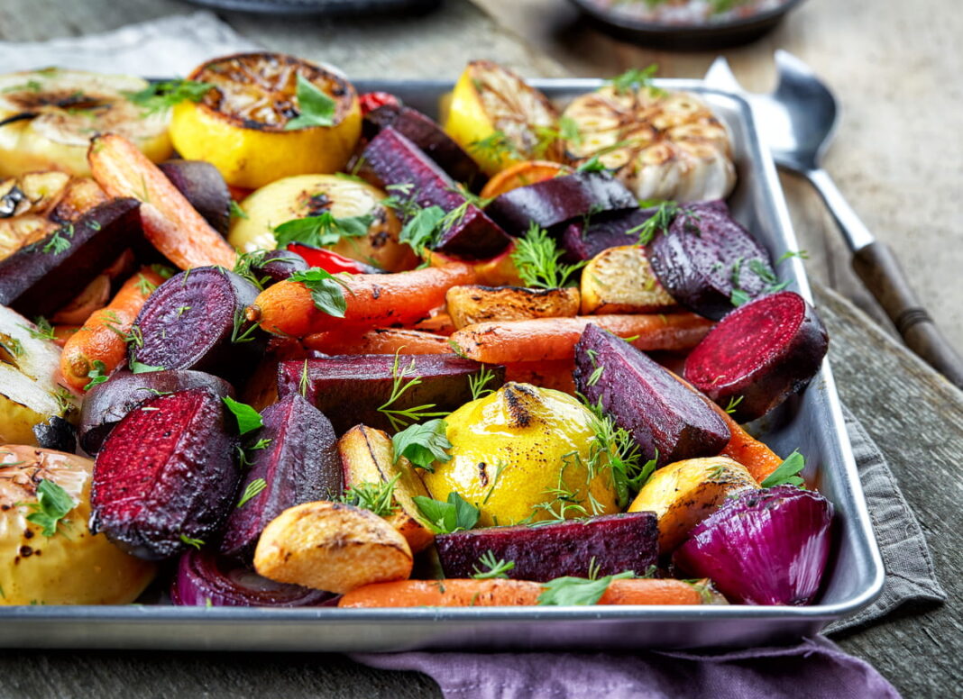 tray of colourful roasted vegetables, including beetroot, carrot, potato, onion and garlic, sprinkled with fresh green herbs