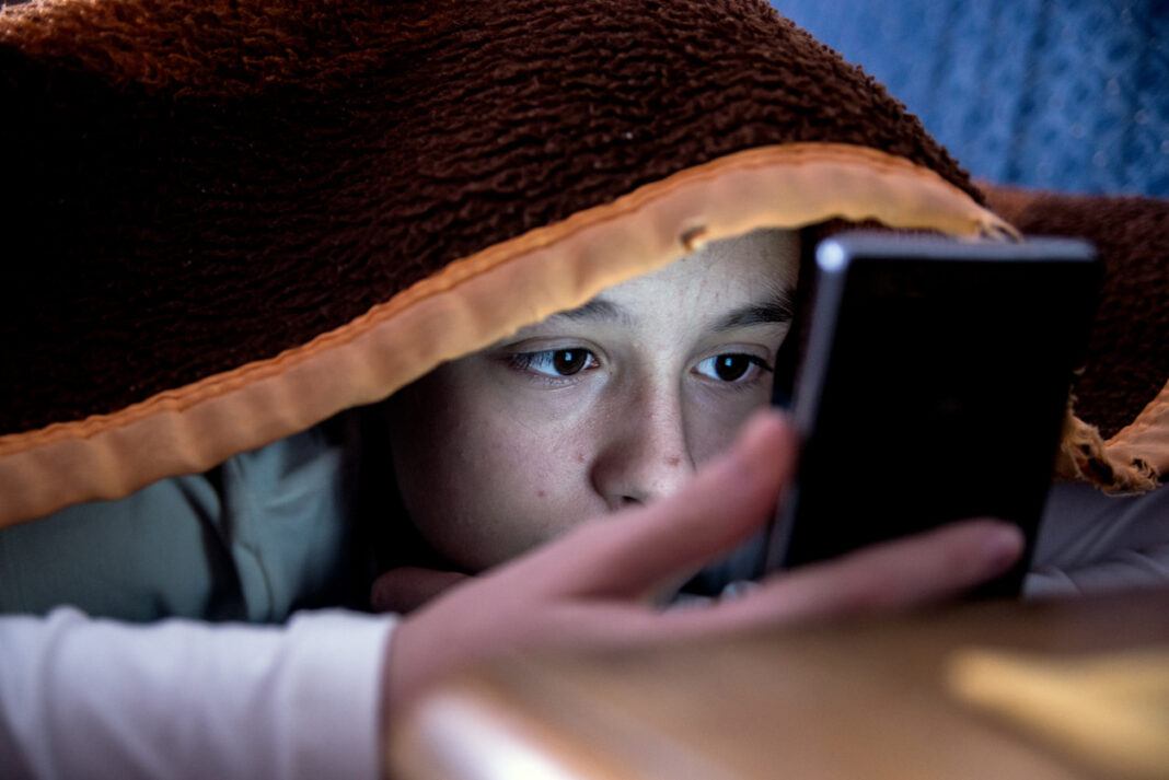teenager on mobile phone in bed at night