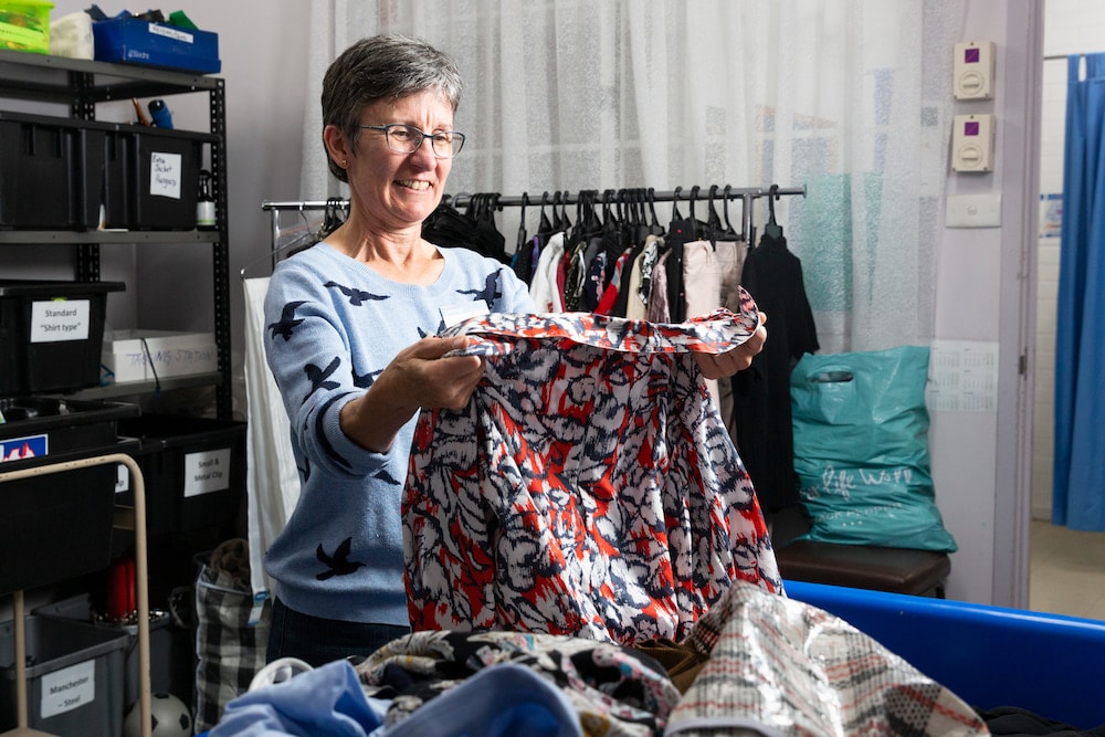 An op shop employee holds up a shirt from a charity bin, assessing its suitability.