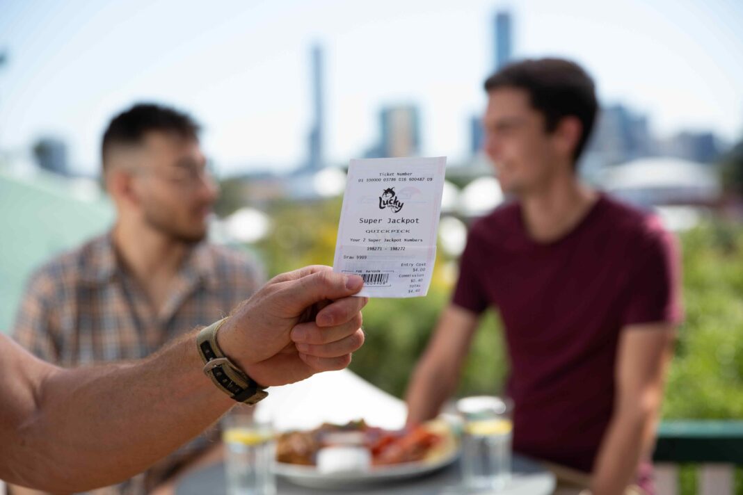 male hand holding a lottery ticket with two other men and city skyline blurred in the background