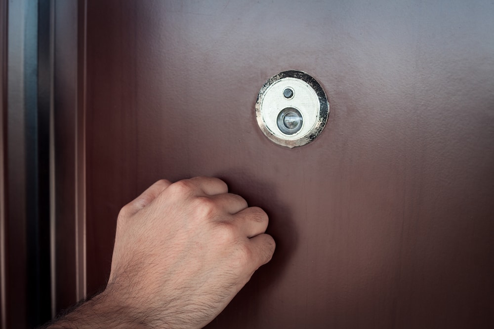 A white male hand knocks on a brown door, to symbolise the door knocking occurring in Weston Creek.