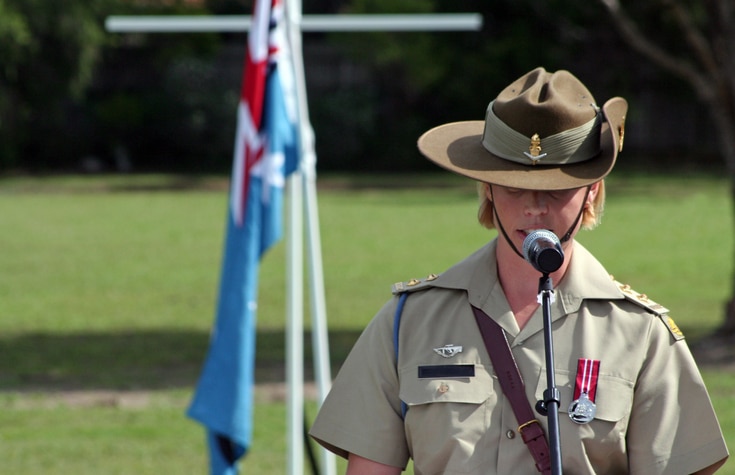 A young female Australian Army officer wearing full ceremonial uniform, traditional Sam Browne belt and the Australian Defence Medal gives a speech outdoors at an ANZAC Day ceremony