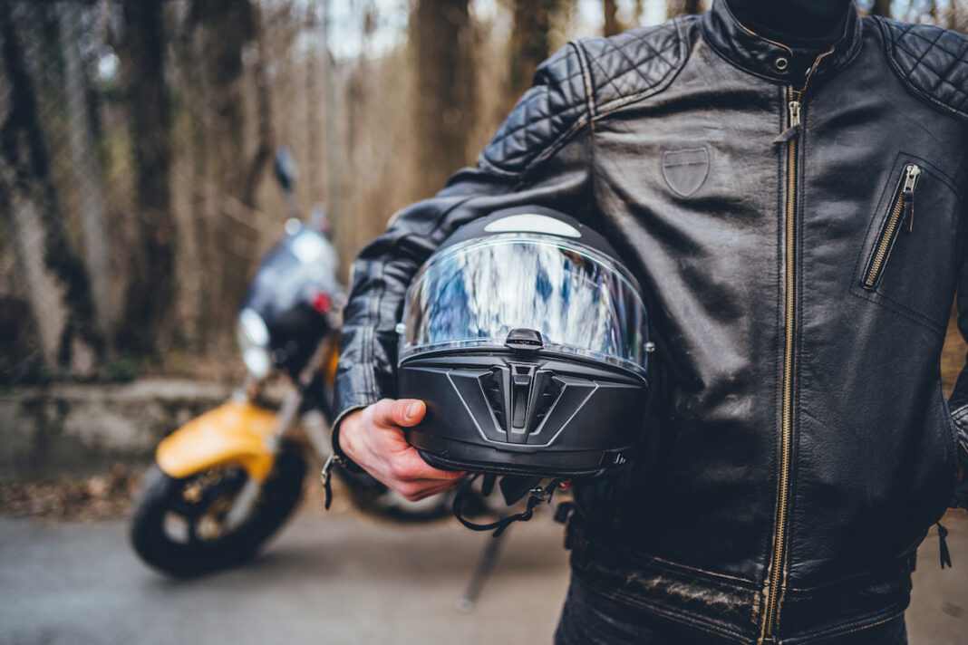 A motorcyclist stands in front of the camera, pictured from below the chin to the waist, holding a helmet against his hip. Today ACT Policing said motorcyclist deaths were overrepresented in ACT.